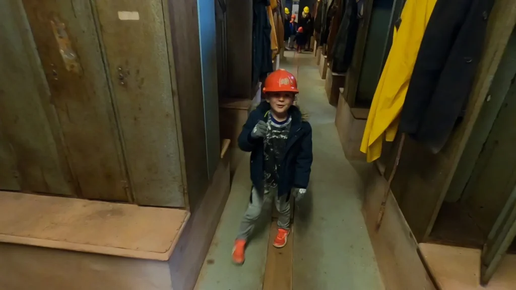 The interior of the miners' dry (changing room) at Geevor Tin Mine, showing rows of metal lockers and baskets suspended from the ceiling by chains.